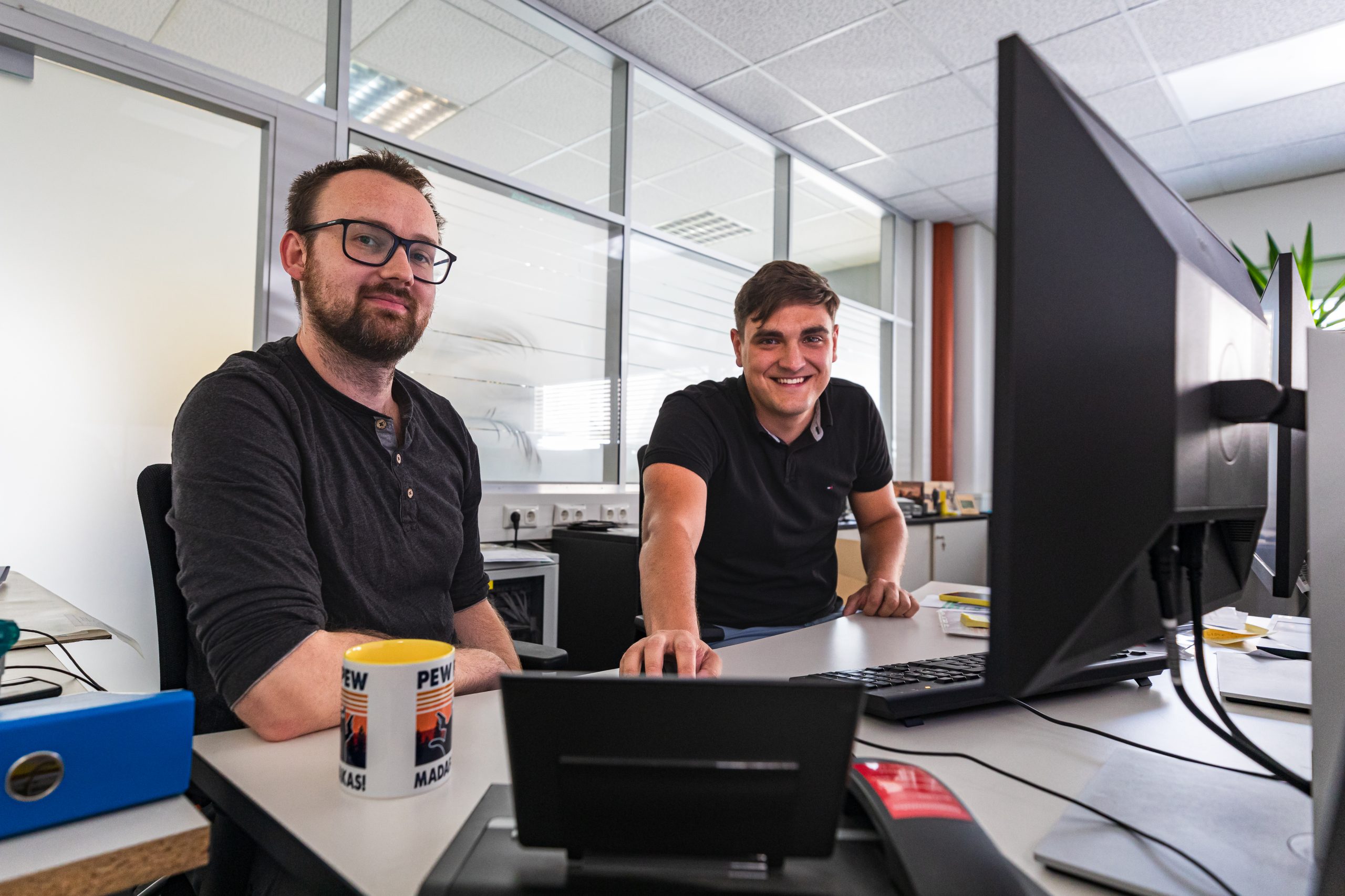 Zwei junge Männer im Büro vorm Bildschirm am Computer bei einer Schulung